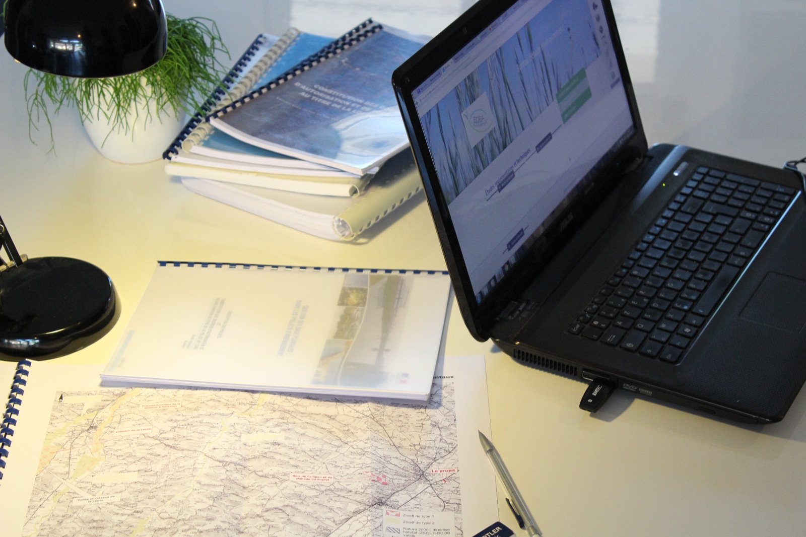 Plan de travail : rapports d'étude reliés, ordinateur portable et carte au 1/25 000